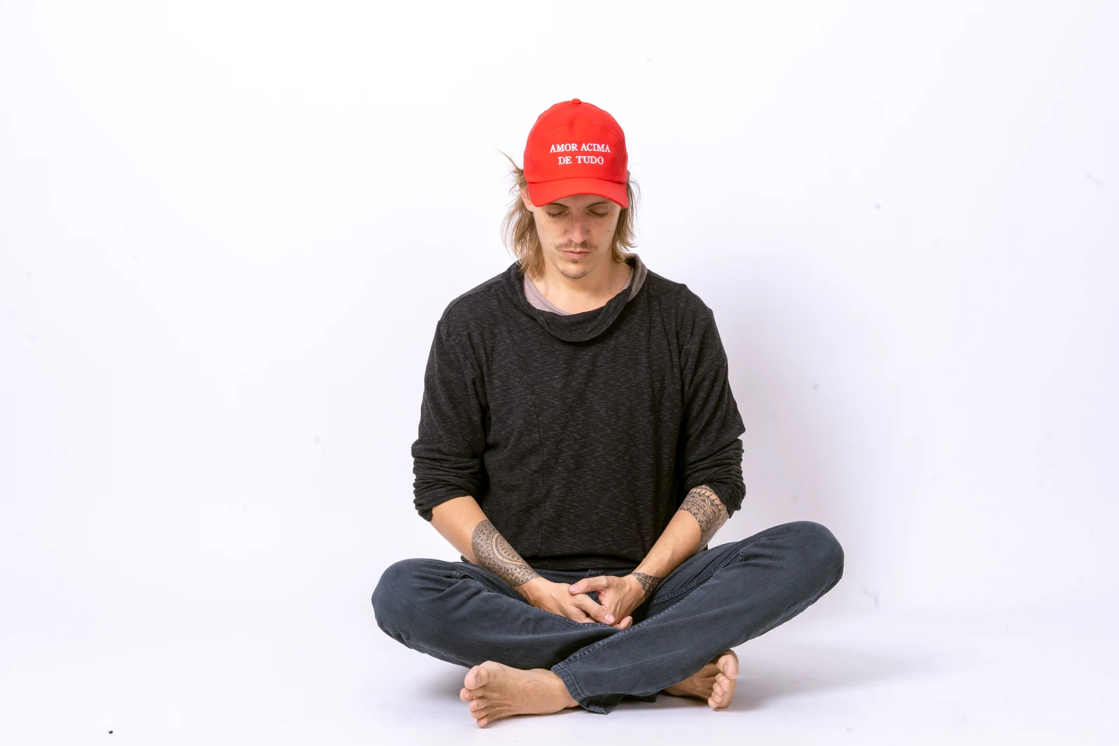 A seated figure wearing a red cap embroidered with the words Amor Acima de Tudo.