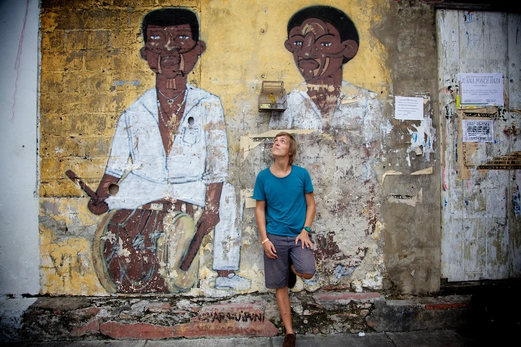 A person in a blue shirt beside painted musicians on a weathered wall in Cartagena.