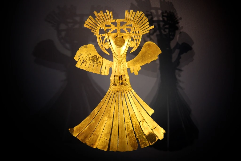 A gold figure with a headdress and outstretched arms on display at Museo del Oro.