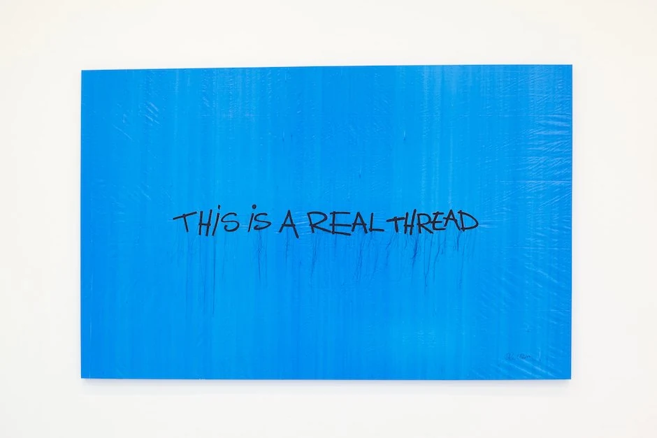 This Is a Real Thread, black lettering and hanging threads on a blue plastic sheet.