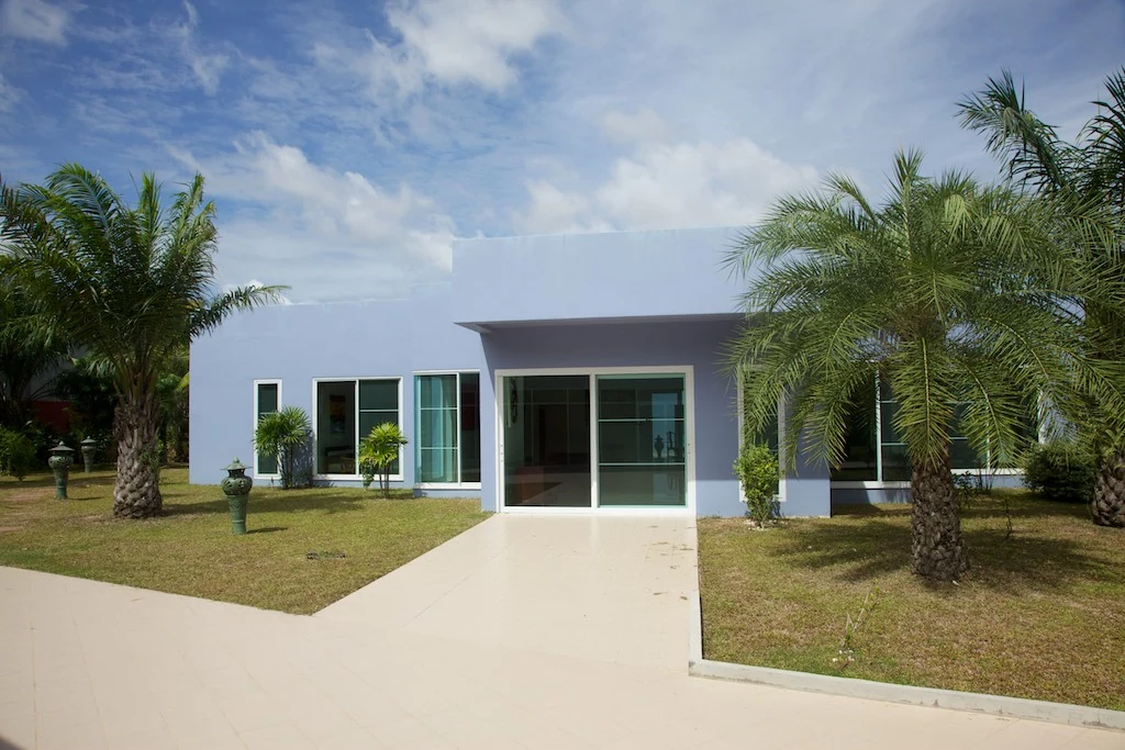 The pale blue Thaillywood residency building surrounded by palm trees.